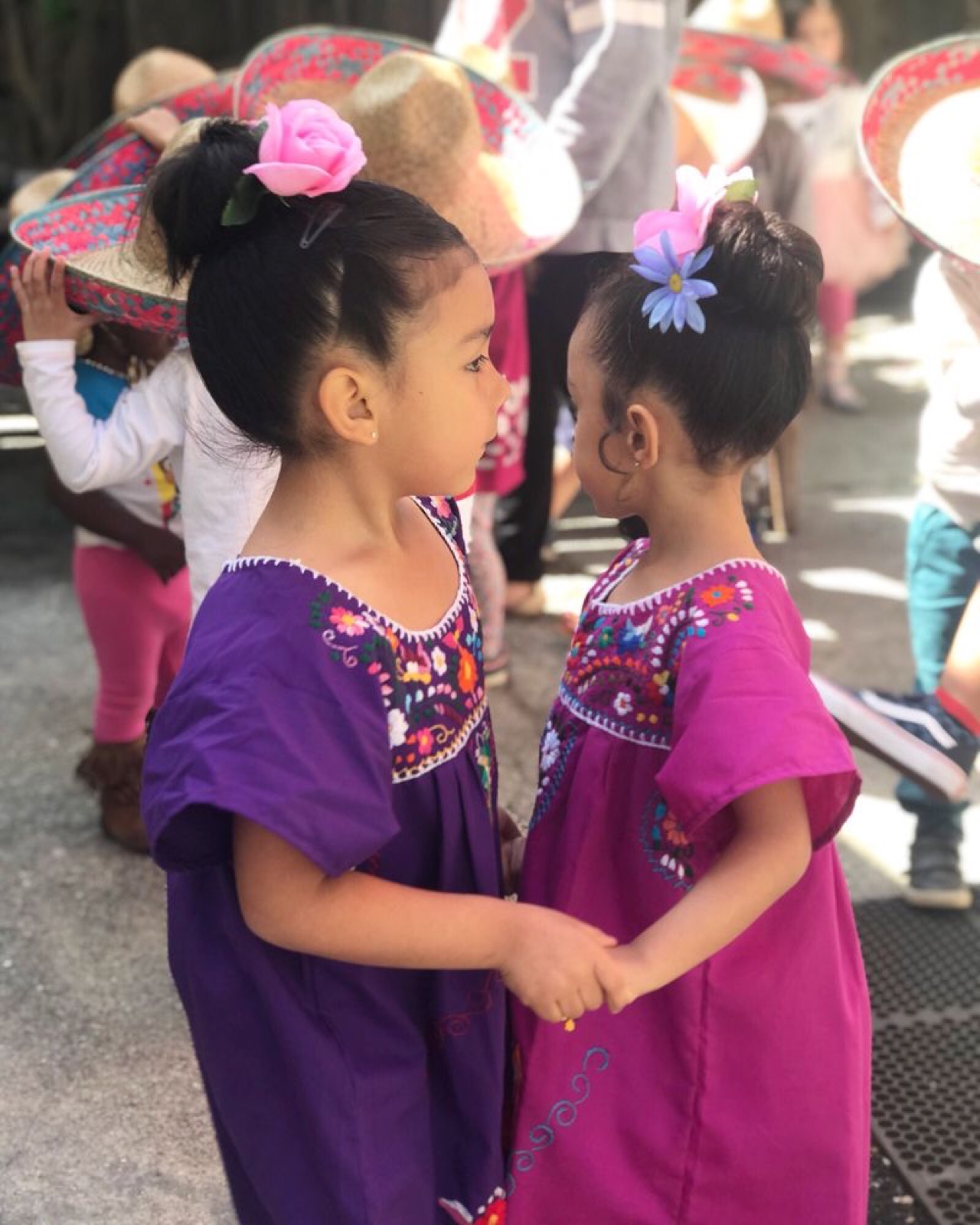 Two young girls in embroidered Mexican dresses holding hands at the Cinco de Mayo celebration