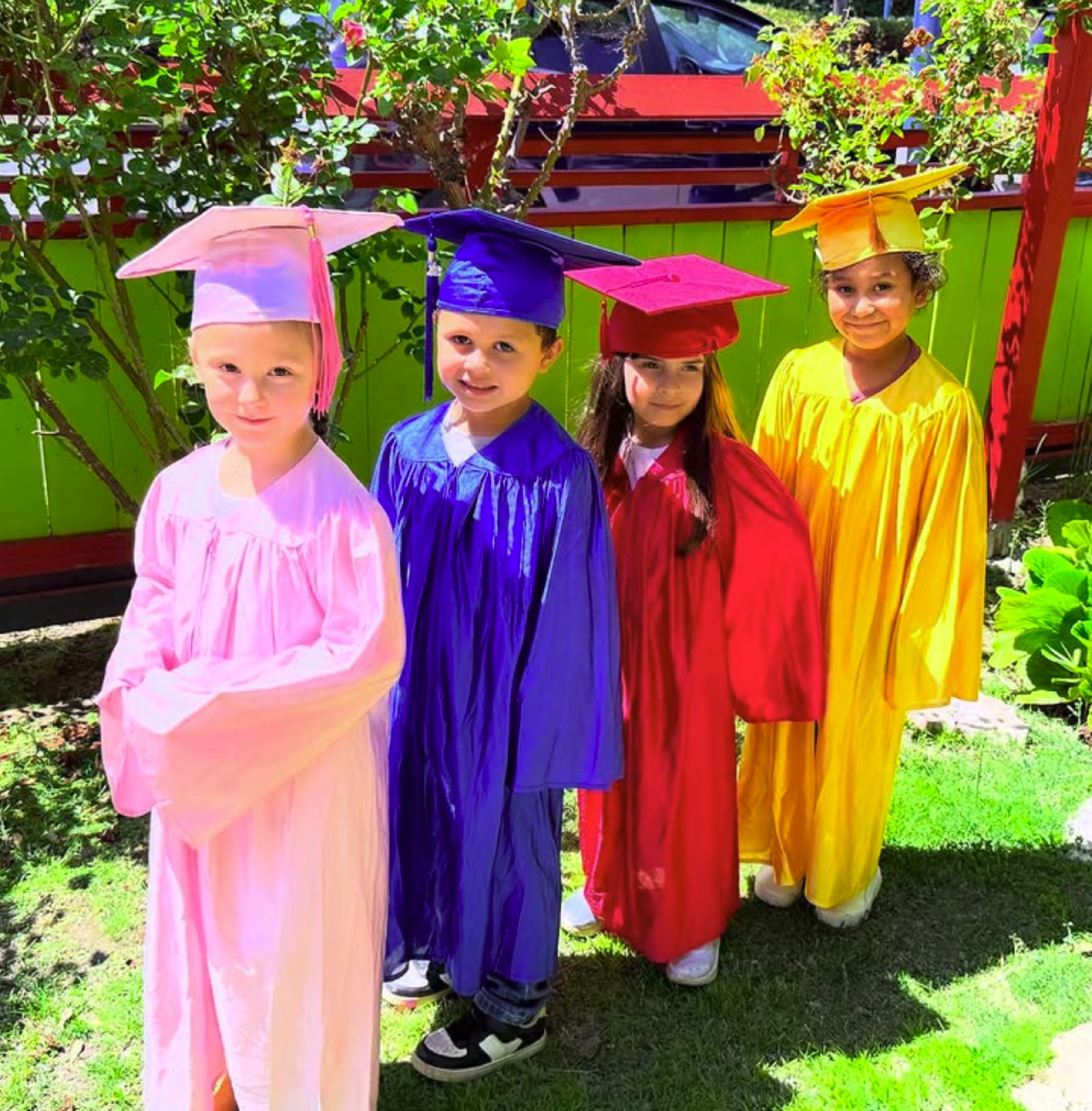 Four proud graduates in bright caps and gowns in the school garden