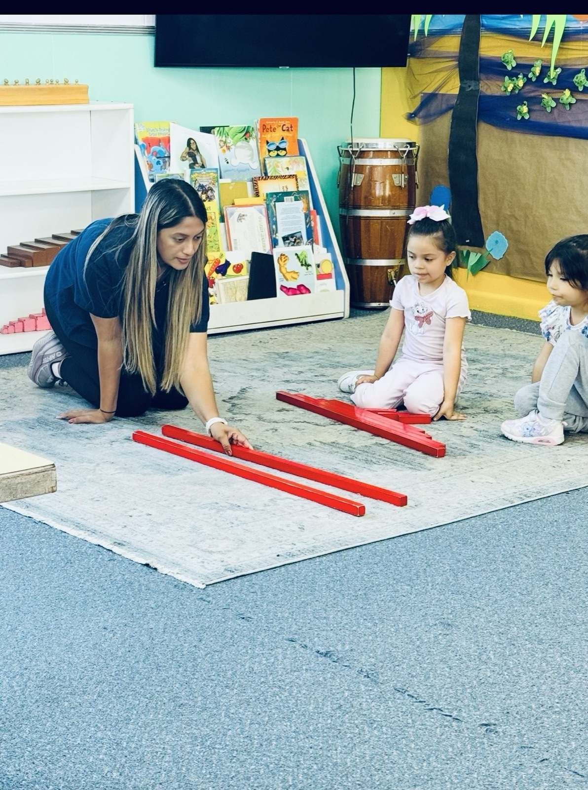 A teacher presenting the red number rods to two young students