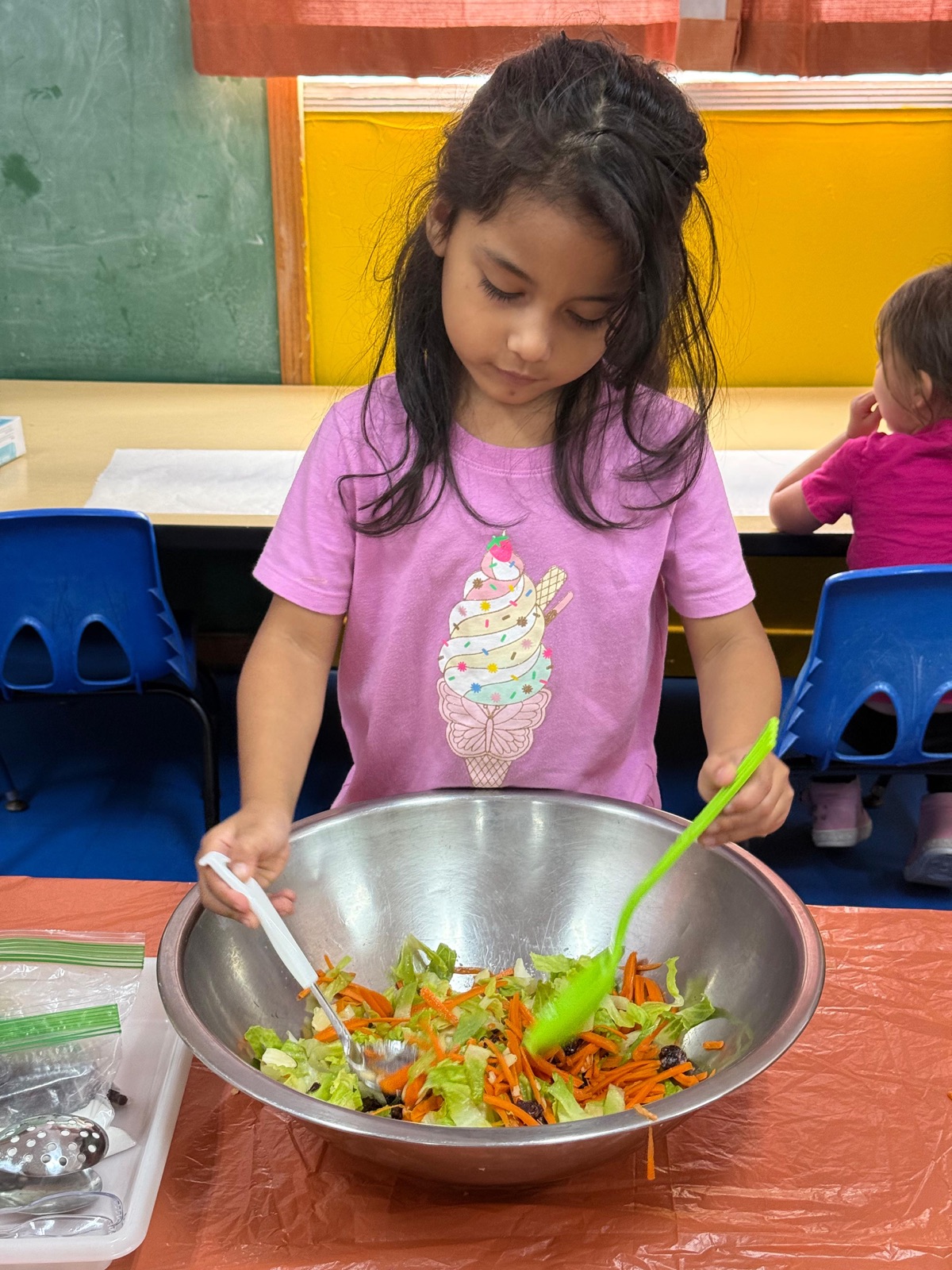 A girl tosses a big bowl of salad the class prepared together